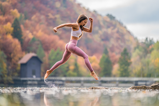 Young woman jumping over water in the nature