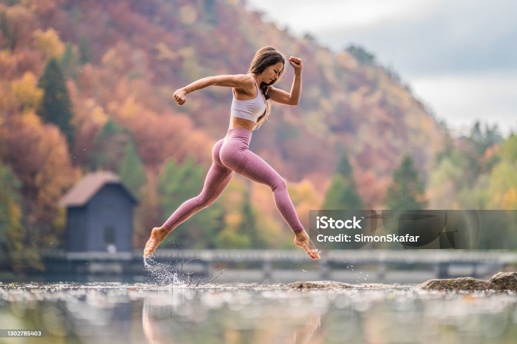 Young woman jumping over water in the nature Young woman jumping over lake water during autumn Exercising Stock Photo