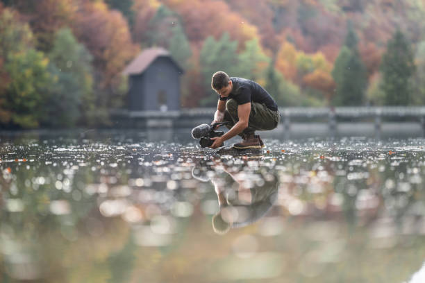 Young man photographing with camera over water in lake