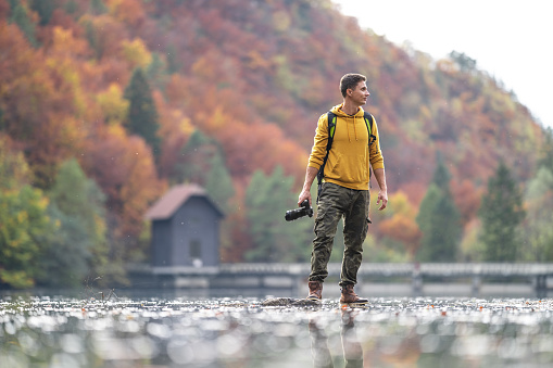 Young male photographer looking away while holding camera in lake