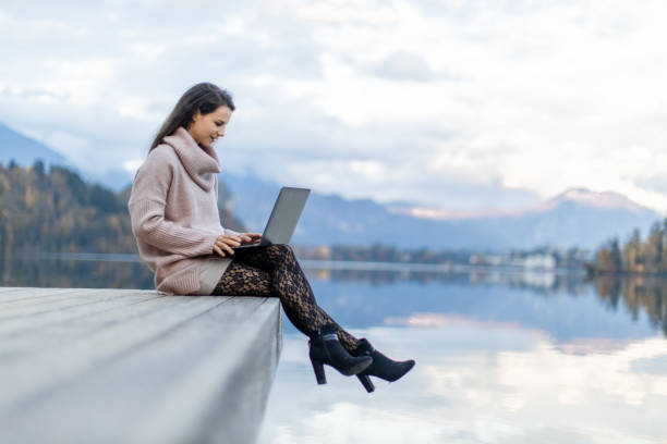 istock Young woman working on laptop beside lake 1302785527