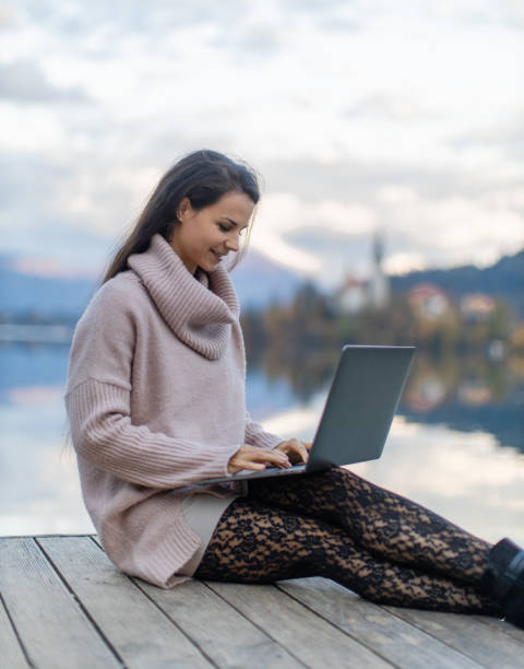 istock Young woman working on laptop beside lake 1302785539