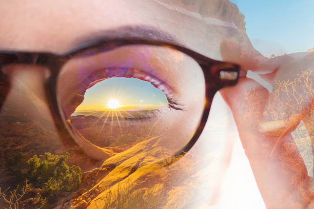 Double exposure image of sunset over landscape in woman eye through eyeglasses