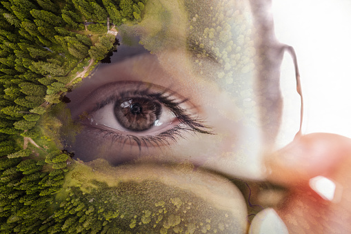 Double exposure of young woman holding eyeglasses superimposed with lake surrounded by trees in forest
