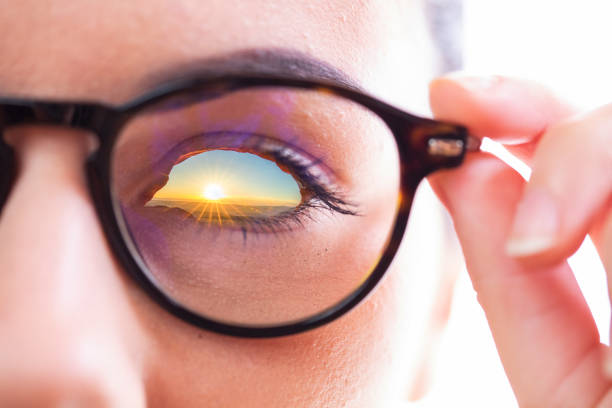 Double exposure of sunset over landscape in woman eye through eyeglasses