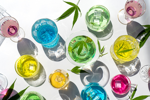 Colorful marijuana infused summer cocktails in various rainbow colors on white background with strong shadows top view