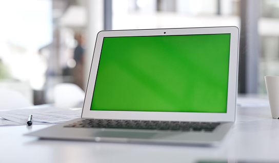 Shot of a laptop with a green screen on a desk in a modern office