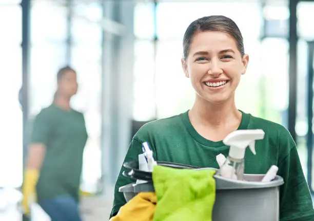 Portrait of a young woman cleaning an office with her colleague in the background