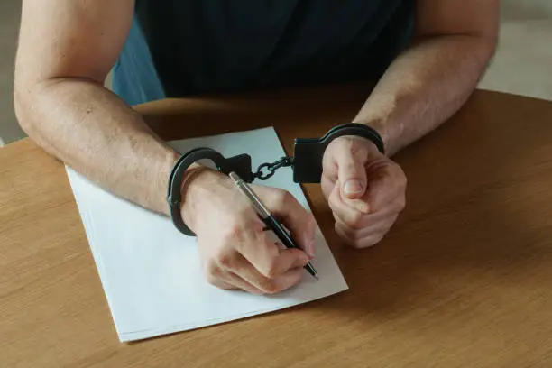 Men hands with handcuffs fill the police record, confession. on top of the police investigative detective. Arrest, bail, criminal, prison. fingerprints, criminal