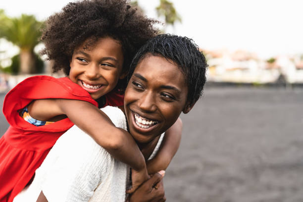 felice famiglia africana che si diverte sulla spiaggia durante le vacanze estive - madre e figlia afro che si godono le vacanze - i genitori amano e il concetto di stile di vita di viaggio - child caribbean black latin american and hispanic ethnicity foto e immagini stock