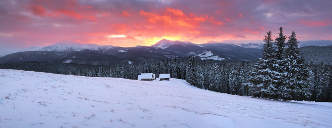 Amazing sunrise. Winter forest. Old wooden huts on the lawn covered with snow. High mountains with snow white peaks. Wallpaper background. Location place Carpathian, Ukraine, Europe.