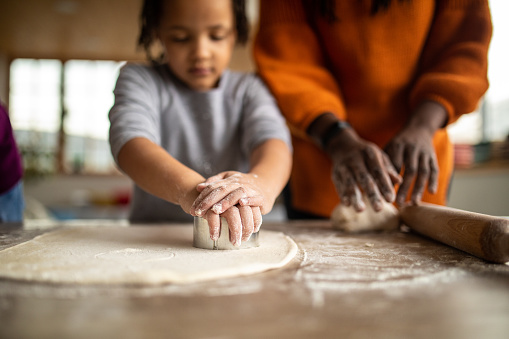 Sisters helping mother to prepare dough in kitchen at home