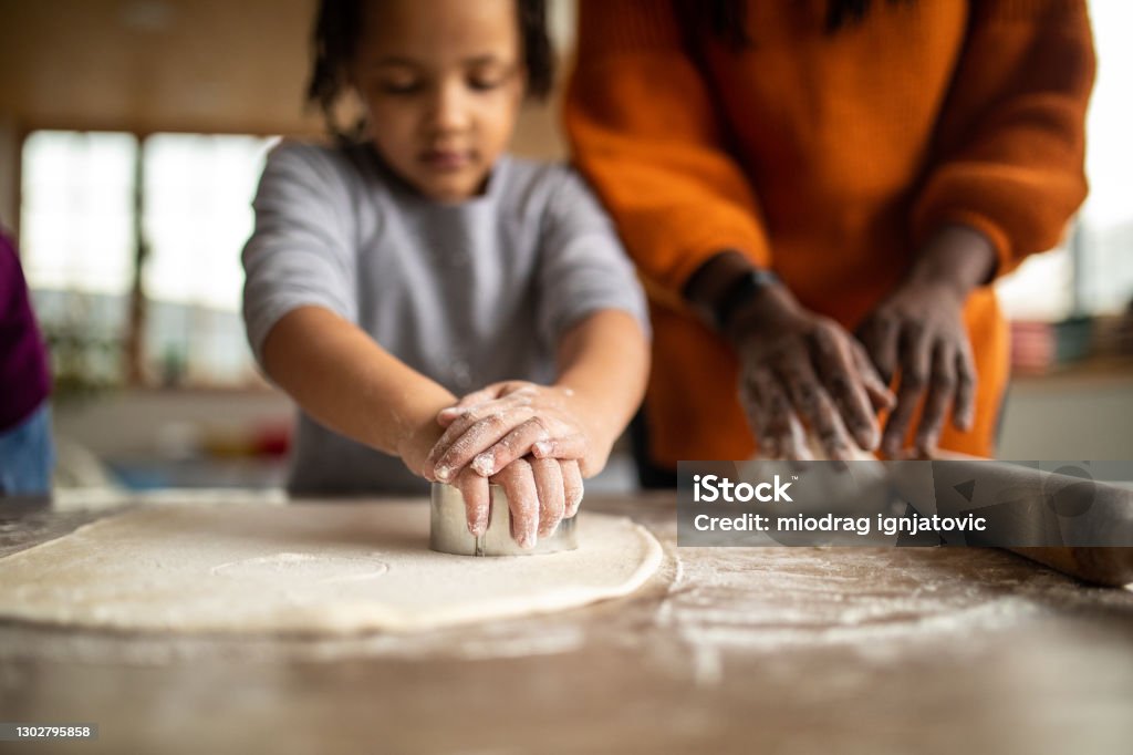 Sisters helping mother to prepare dough in kitchen at home Cookie Stock Photo