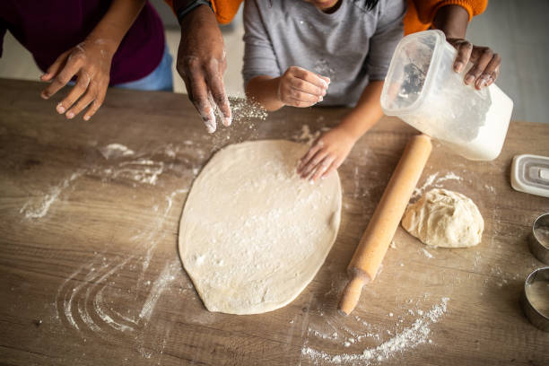 istock Two sisters bonding with their mother while preparing dough in kitchen at home 1302795905