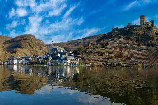 Traditional German village among the hills covered with vineyards on the riverbank of the Mosel river.