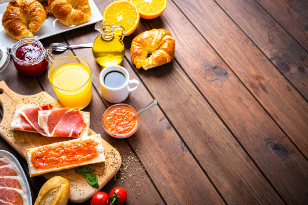Mediterranean breakfast on wooden table. High angle view Spanish tomato and ham toast, croissant, coffee, orange juice. Traditional Mediterranean breakfast or lunch on wooden table. The composition is at the left of an horizontal frame leaving useful copy space for text and/or logo at the right. High angle view. High resolution 42Mp studio digital capture taken with SONY A7rII and Zeiss Batis 40mm F2.0 CF lens spanish breakfast stock pictures, royalty-free photos & images