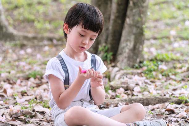 istock Cheerful kid boy looking plasticine holding in his hands while sitting in the park. Little mixed race schoolchild with plasticine in his hands while playing alone on nature background. 1302803583