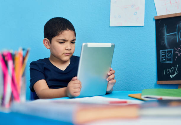 I don't get it... Shot of an adorable little boy using a digital tablet to complete a school assignment at his desk myopia stock pictures, royalty-free photos & images