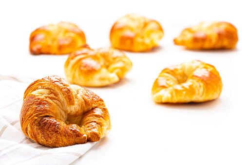 Close up view of fresh homemade croissants isolated on white background. Selective focus on foreground. Predominant colors are yellow and white. High resolution 42Mp studio digital capture taken with Sony A7rII and Sony FE 90mm f2.8 macro G OSS lens