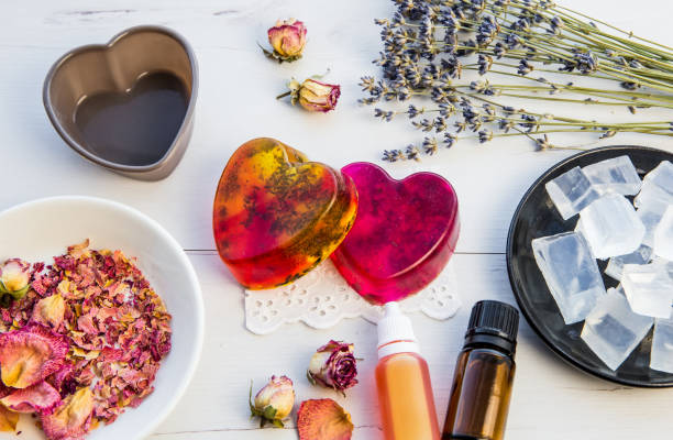 istock Making handmade soap with crystal clear melt and pour soap mixture. Ready to use pink and yellow tied soaps with rose petals and lavender blossoms in center surrounded by ingredients. 1302808864