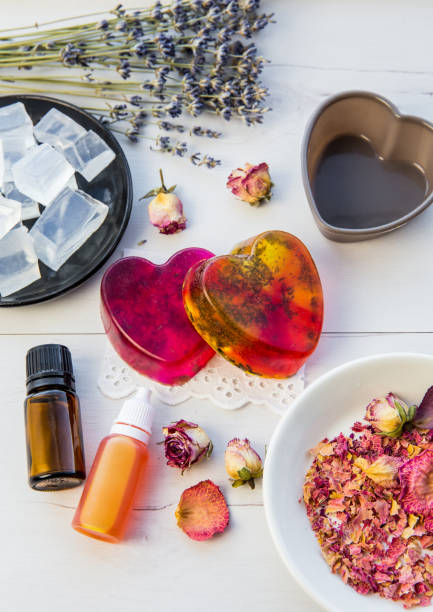 istock Making handmade soap with crystal clear melt and pour soap mixture. Ready to use pink and yellow tied soaps with rose petals and lavender blossoms in center surrounded by ingredients. 1302808880