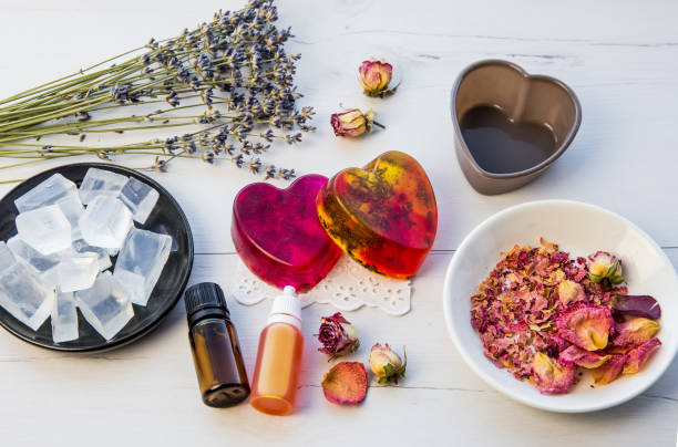 istock Making handmade soap with crystal clear melt and pour soap mixture. Ready to use pink and yellow tied soaps with rose petals and lavender blossoms in center surrounded by ingredients. 1302808900