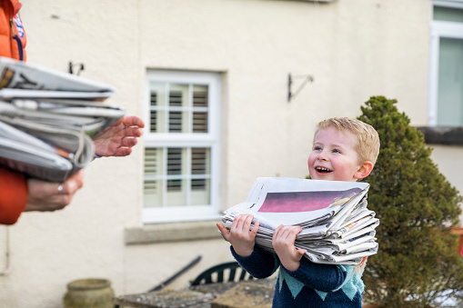 Mother helping her young son recycle newspapers at their home in the North East of England. They are carrying stacks of them.