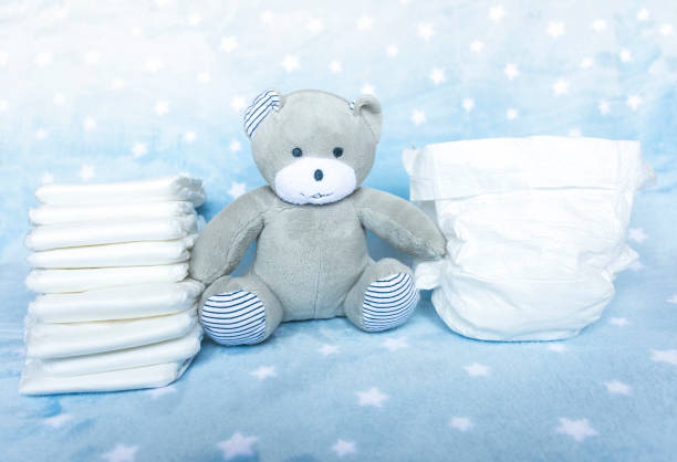 istock Stack of white disposable diapers for little babies on blue background with stars and cute teddy bear. Selective focus 1302810699