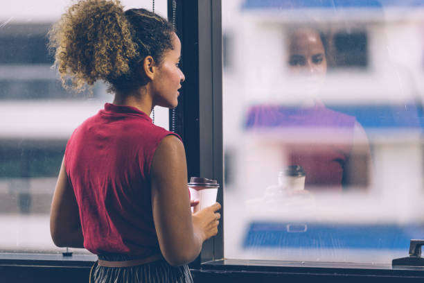 istock Woman holding coffee cup and looking out office building 1302812169