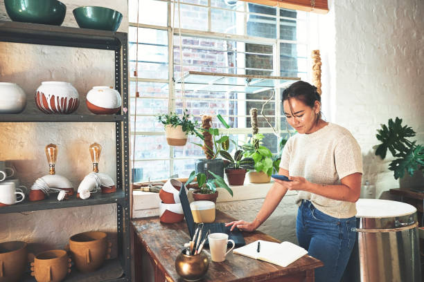 This customer wants something specific Cropped shot of an attractive young business owner standing and using her laptop and cellphone in her pottery studio pottery photos stock pictures, royalty-free photos & images