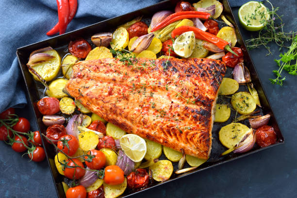 Baked salmon fillet with vegetables Large juicy salmon fillet with a chili honey marinade, baked with vegetables and served hot from the oven on a baking sheet baking sheet stock pictures, royalty-free photos & images