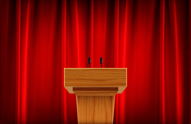 istock Wooden announcement podium with microphone on red curtain background 1302814770