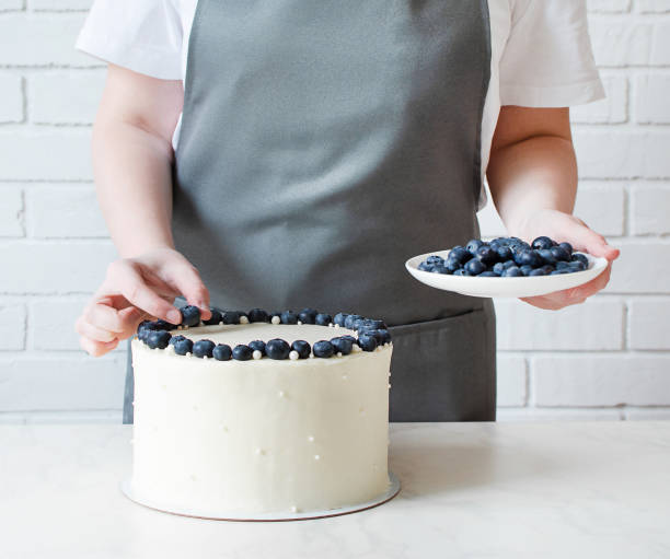 istock White cake with cream cheese and fresh blueberries. Confectioner decorating wedding cake with berries. 1302816446
