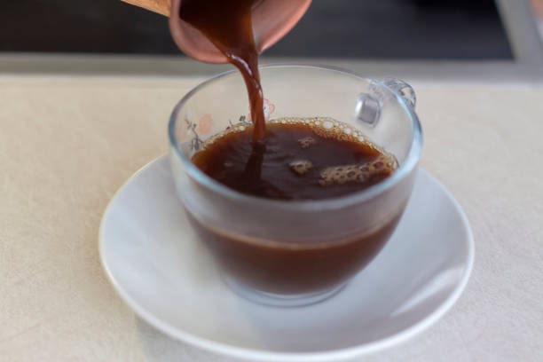 istock Black freshly brewed coffee is poured from a copper cup into a cup. 1302817818