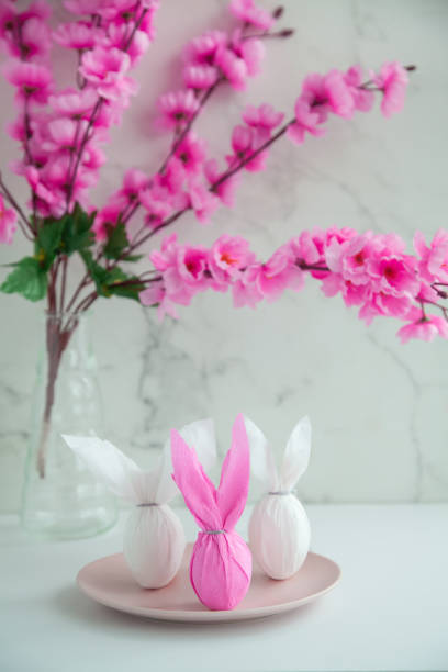 istock Three eggs bunny in a colored paper wrapper on a plate and table in a cherry blossoms. The Easter holiday 1302818428