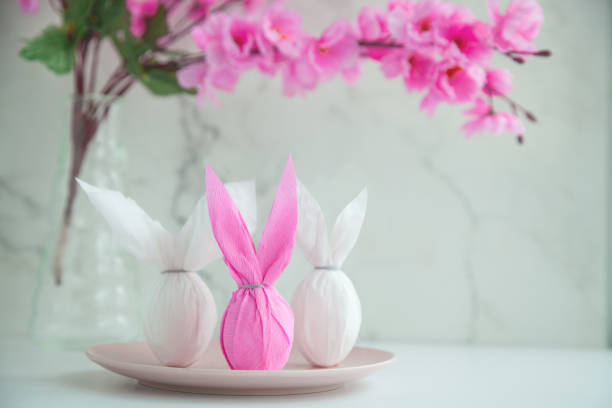 Three eggs bunny in a colored paper wrapper on a plate and table in a cherry blossoms. The Easter holiday
