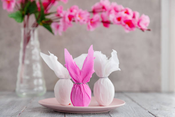 istock Three eggs bunny in a colored paper wrapper on a plate and wooden table in a cherry blossoms. The Easter holiday 1302818439