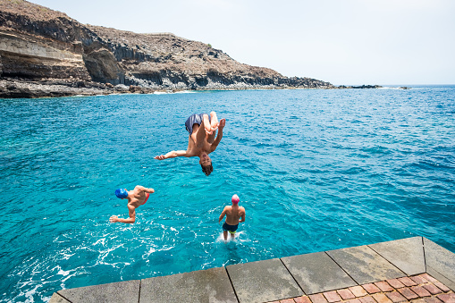 group of friends jumping off together at the beach doing flips and having fun in the water - people enjoying holiday at the beach playing and laughing