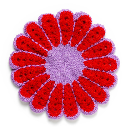 Homemade crocheted napkin in the form of a round flower with red petals on a light background. Handicraft masterclass