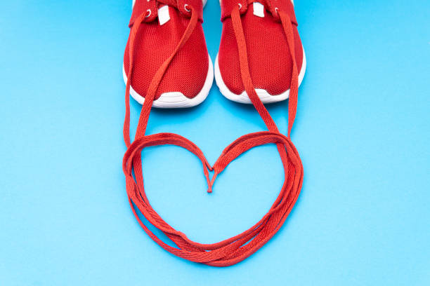 Crop view of red athletic sneakers and a heart symbol made of the shoelaces on a blue background. Running passion creative concept. shoe shoelace heart shape love stock pictures, royalty-free photos & images