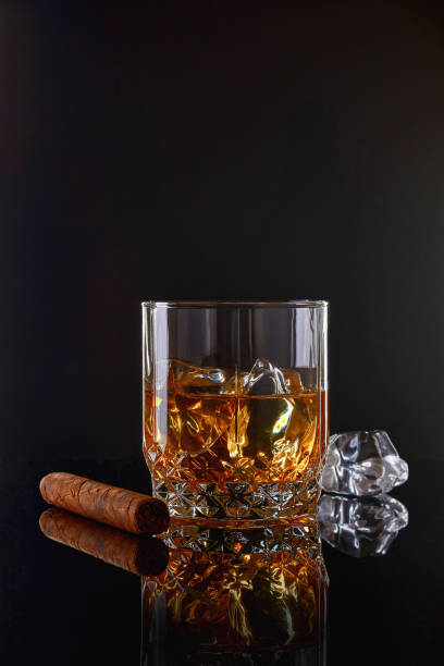 whiskey with ice or brandy in glass with cigar on black background. whisky with ice in glass. whiskey or brandy. selective focus. - cigar whisky bar cognac imagens e fotografias de stock
