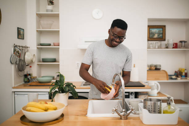 glücklicher afroamerikanischer mann, der zu hause geschirr wäscht - abwaschen stock-fotos und bilder