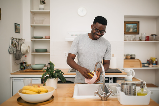 Young happy African American man washing dishes at home, and smiling
