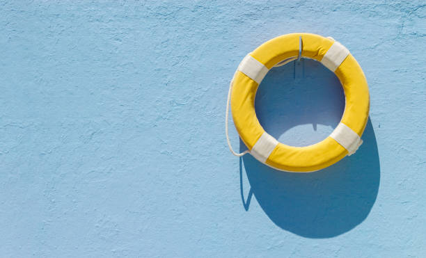 Yellow circular lifebuoy hanging on blue wall with copy space stock photo