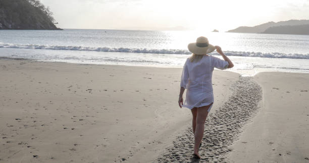 istock Woman walks down sandy beach at sunrise 1302830980