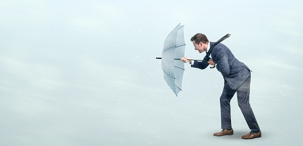 Businessman opposing a strong wind with an umbrella. Conceptual image depicting adversity in business life.