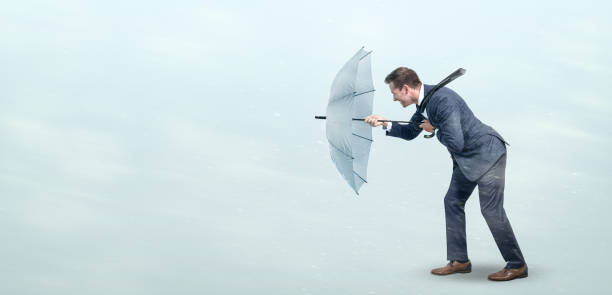 Businessman defying strong headwind Businessman opposing a strong wind with an umbrella. Conceptual image depicting adversity in business life. resilience stock pictures, royalty-free photos & images