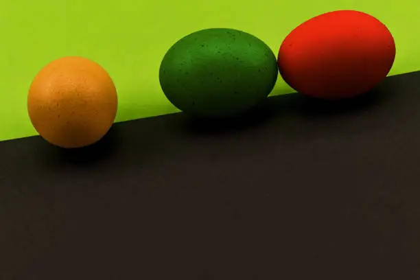 Abstract picture at Easter, three eggs on the oblique borderline of a front black and rear green background, concept