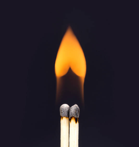 Photo of Heart shaped flame coming from a pair of burning matchsticks on a black background.