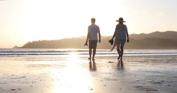istock Mature couple walks down sandy beach at sunrise 1302832659